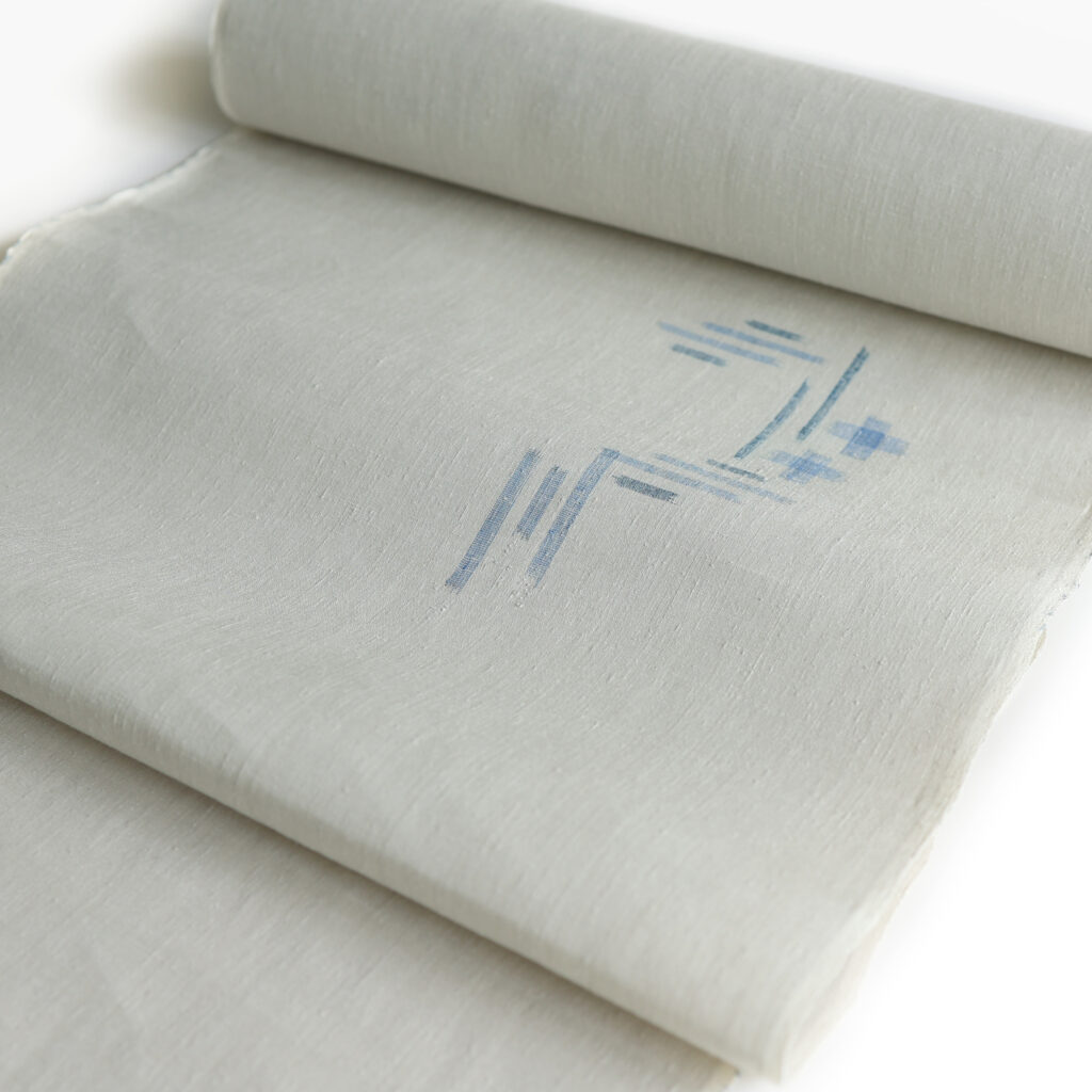 うすいグレー地の本場結城紬の反物。飛び柄の絣模様は青系の色でさわやか。